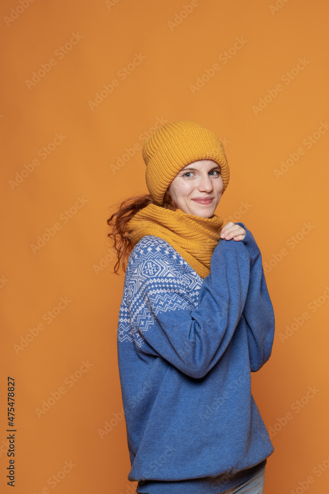 young red-haired girl in a warm hat and a knitted sweater on a yellow background young red-haired girl in a warm hat and a knitted sweater on a yellow background