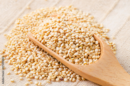 Raw, whole, unprocessed quinoa seed in wooden spoon.