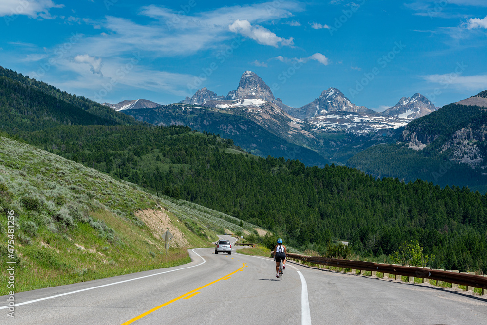 Fototapeta premium USA, Wyoming. Cyclist and car on highway with view of Grand Teton, west side of Teton Mountains