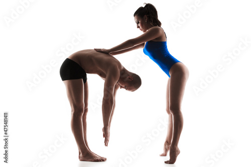 Female trainer helping guy to stretching back, isolated on white background