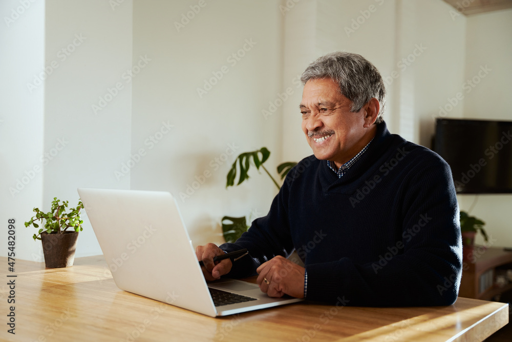Multi-cultural elderly male smiling while on online call with family. Isolating in modern home, sitting at kitchen counter top. Multi-cultural elderly male smiling while on online call with family. Isolating in modern home, sitting at kitchen counter top.