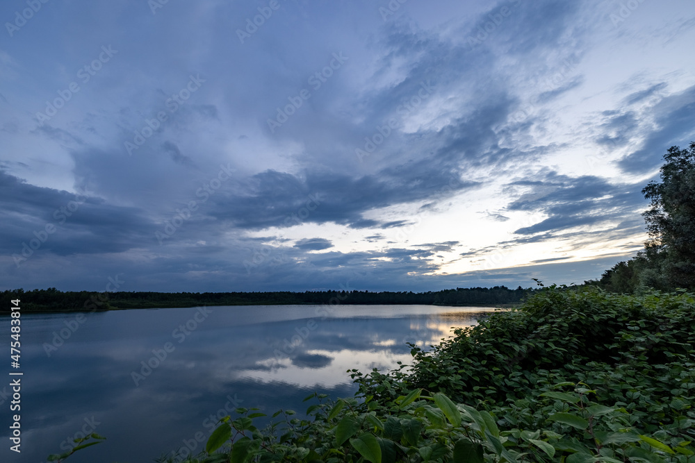 a beautiful blue lake with green tree in the foreground under a dramatic blue dusk sky. High quality photo