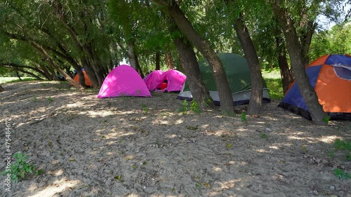 Panning shot of the colorful camping tents under the trees in the forest on the sand beach of river Dniester (Dnestr) in Transnistria, Moldova, sunn photo