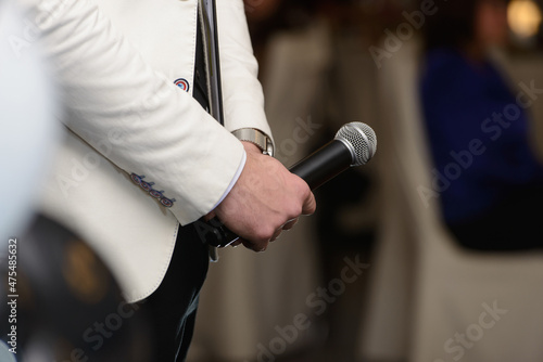 Business and speech topic: Man in a white jacket holding a black microphone. Vertical photo