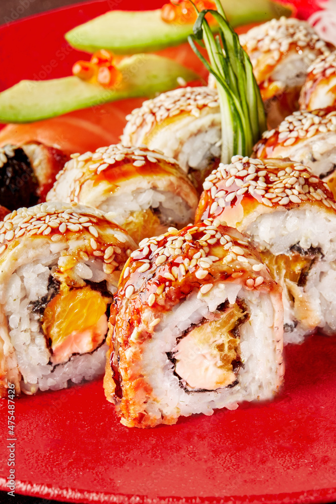Closeup of unagi rolls with grilled eel, cream cheese, orange pulp and sesame on red plate