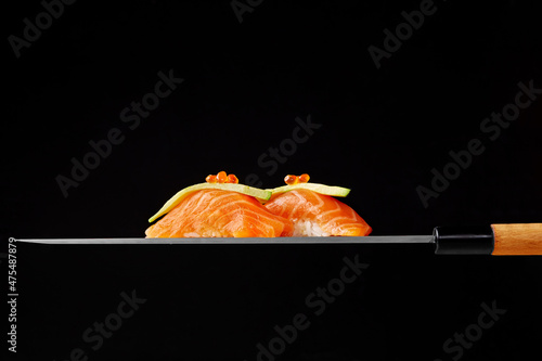 Nigiri sushi with raw salmon, avocado and red caviar on blade of Japanese knife