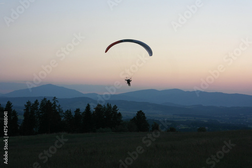 Fly paragliding adventure, flight soaring in the clouds. Freedom ambience - wind air, stunning view hill valley panorama, pink horizon gradient, aesthetics of evening mountain Tatra, Poland. 