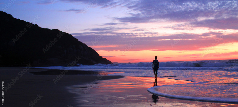 Homem não identificado caminhando próximo ao mar no nascer do sol em florianopolis, santa Catarina