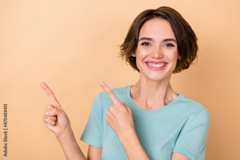 Photo of young pretty girl indicate fingers empty space ads decide suggest discount isolated over beige color background Photo of young pretty girl indicate fingers empty space ads decide suggest discount isolated over beige color background