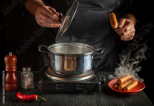 Chef cooks Vienna sausage in a saucepan. Working environment in the restaurant kitchen. Delicious breakfast or dinner photo