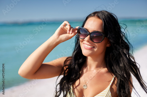 people, summer and swimwear concept - happy smiling young woman in sunglasses and bikini swimsuit on beach