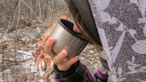 A girl in autumn in nature by the campfire drinks warm coffee from a mug photo