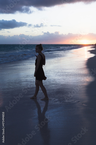 A girl walks the beach in the sunrise, silhouette