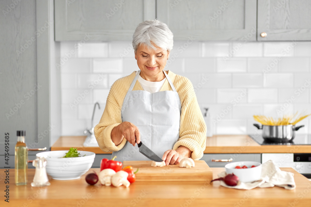healthy eating, food cooking and culinary concept - happy smiling senior woman with knife chopping champignons on kitchen at home healthy eating, food cooking and culinary concept - happy smiling senior woman with knife chopping champignons on kitchen at home