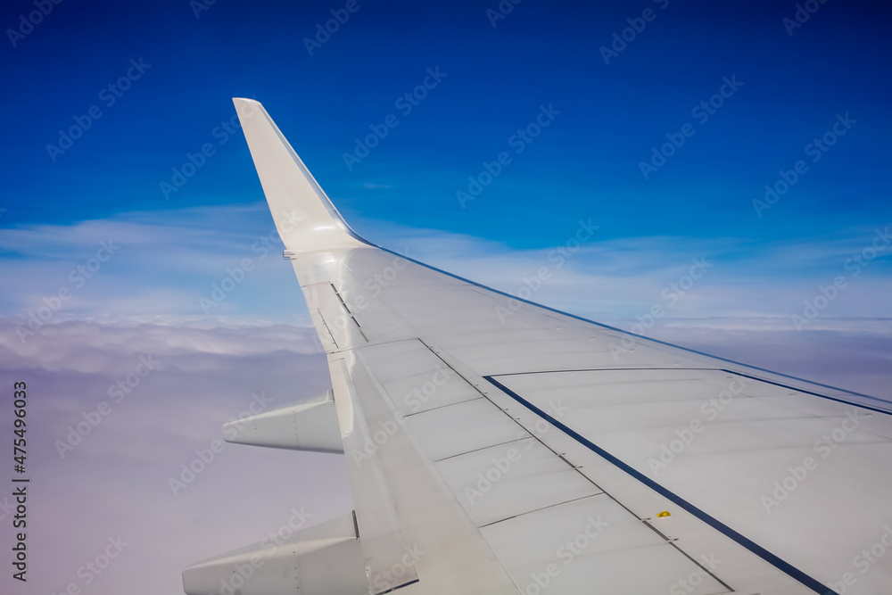 Plane window view with blue sky and clouds.