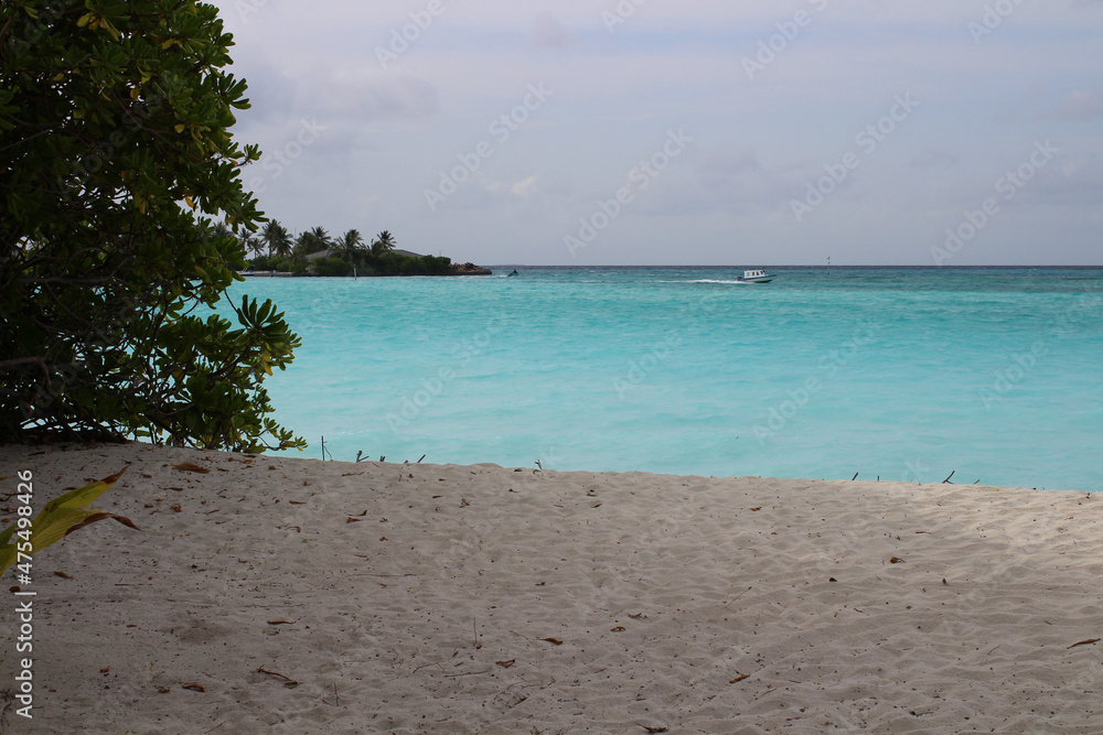 A day in the Maldives, the coast of the Indian Ocean with white sand and corals, a boat is sailing in the azure water