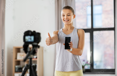 fitness, sport and video blogging concept - happy smiling teenage girl or blogger with camera on tripod and smartphone recording online gym class at home