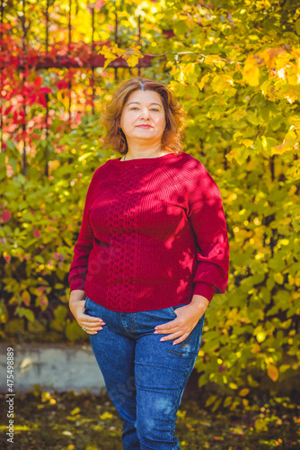Chubby sunny woman in warm casual clothes in city park. Clothes for plus size ladies