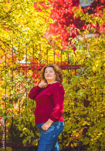 Chubby sunny woman in warm casual clothes in city park. Clothes for plus size ladies