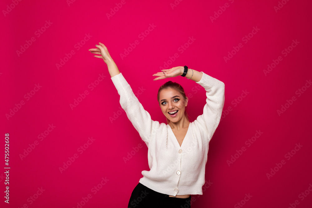 Photo of a beautiful pretty amazing positive smiling happy young blonde woman with makeup and ponytail in a stylish white knitted sweater and black pants having fun and dancing isolated on a pink Photo of a beautiful pretty amazing positive smiling happy young blonde woman with makeup and ponytail in a stylish white knitted sweater and black pants having fun and dancing isolated on a pink