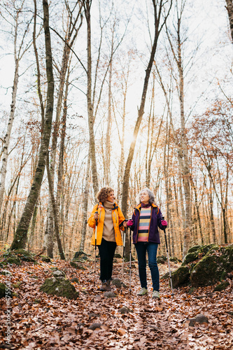 Two senior female friends hiking together through the forest in autumn © Jordi Salas