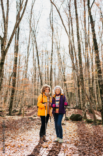 Two senior female friends hiking together through the forest in autumn