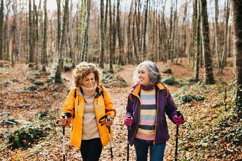 Fotografi Two senior female friends hiking together through the forest in autumn