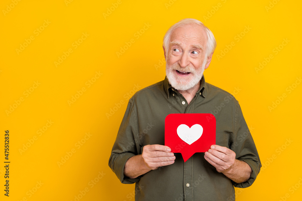 Photo of positive aged man hold like comment card look interested empty space isolated on yellow color background Photo of positive aged man hold like comment card look interested empty space isolated on yellow color background