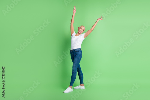 Full size photo of attractive mature woman arms up go wear casual outfit isolated over green color background