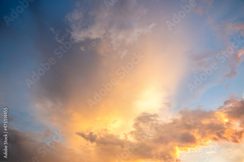 Dramatic cloudscape with puffy clouds lit by orange setting sun and blue sky.