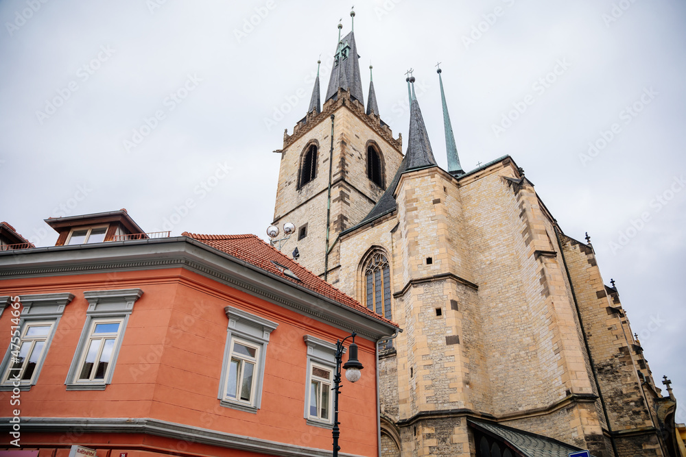 Louny, Czech Republic, 19 September 2021: Medieval catholic stone church of St. Nicholas with gothic high spire clock tower in autumn day, Narrow picturesque street in historic city center, arches