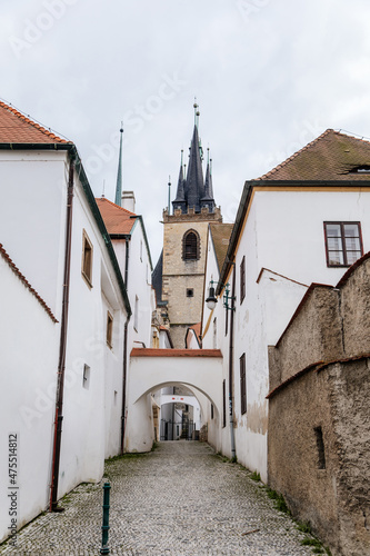 Louny, Czech Republic, 19 September 2021: Narrow picturesque street in historic center in medieval city, spire gothic tower of St. Nicholas church at autumn day, white town buildings, arched passage