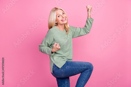 Photo of adorable lucky lady pensioner dressed green pullover walking rising fists isolated pink color background