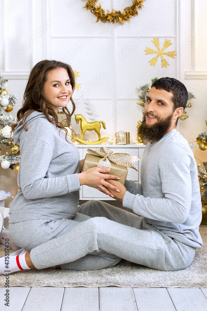 A young couple in gray tracksuits with Christmas gifts. A young guy and a young girl are laughing. Happy guy and girl. Vertical photo. A guy with a real beard. Love couple. A young couple in gray tracksuits with Christmas gifts. A young guy and a young girl are laughing. Happy guy and girl. Vertical photo. A guy with a real beard. Love couple.