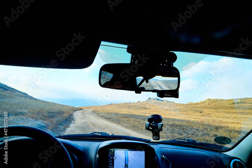 Siberia Baikal, Russia - November 20, 2020: View from of car interior from side of driver to the road and autumn yellow nature landscape with hills through the windshield