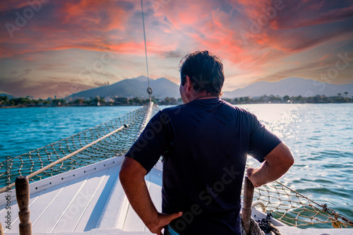 Basilian man watching the sunset on top of a schooner in the city of ubatuba praia itagua in brazil photo