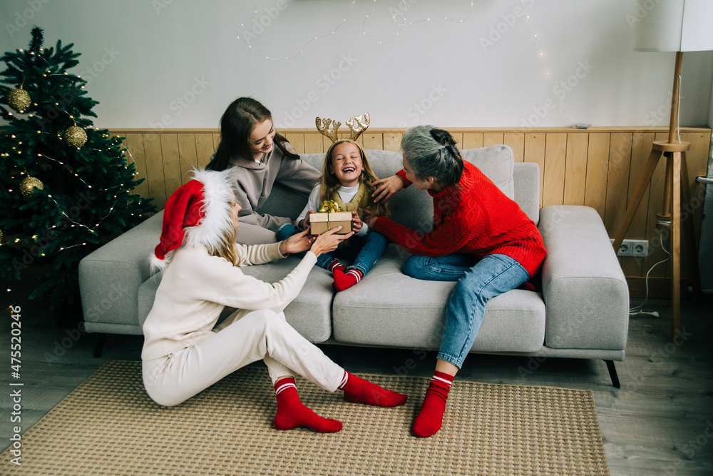 The family celebrate Christmas together. Grandmother, mom and sister give a gift to a little girl. Medium group of people The family celebrate Christmas together. Grandmother, mom and sister give a gift to a little girl. Medium group of people