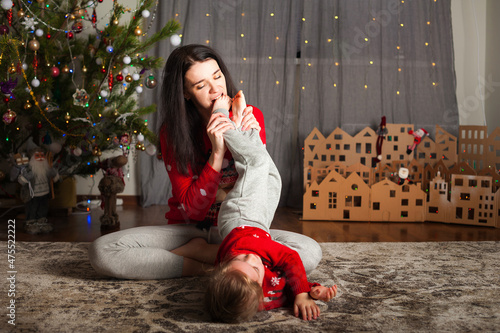 Obraz na plátne Young happy mom and daughter in red sweaters playing, hugging, fooling around at home