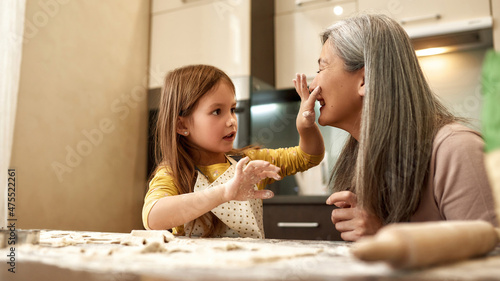 Girl touching face of her grandmother with flour