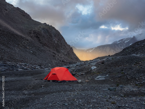 Surrealist alpine landscape with tent on rocky hill among rocks in sunrise. Beautiful morning mountains in low clouds. Surreal scenery with tent in highlands in overcast weather.