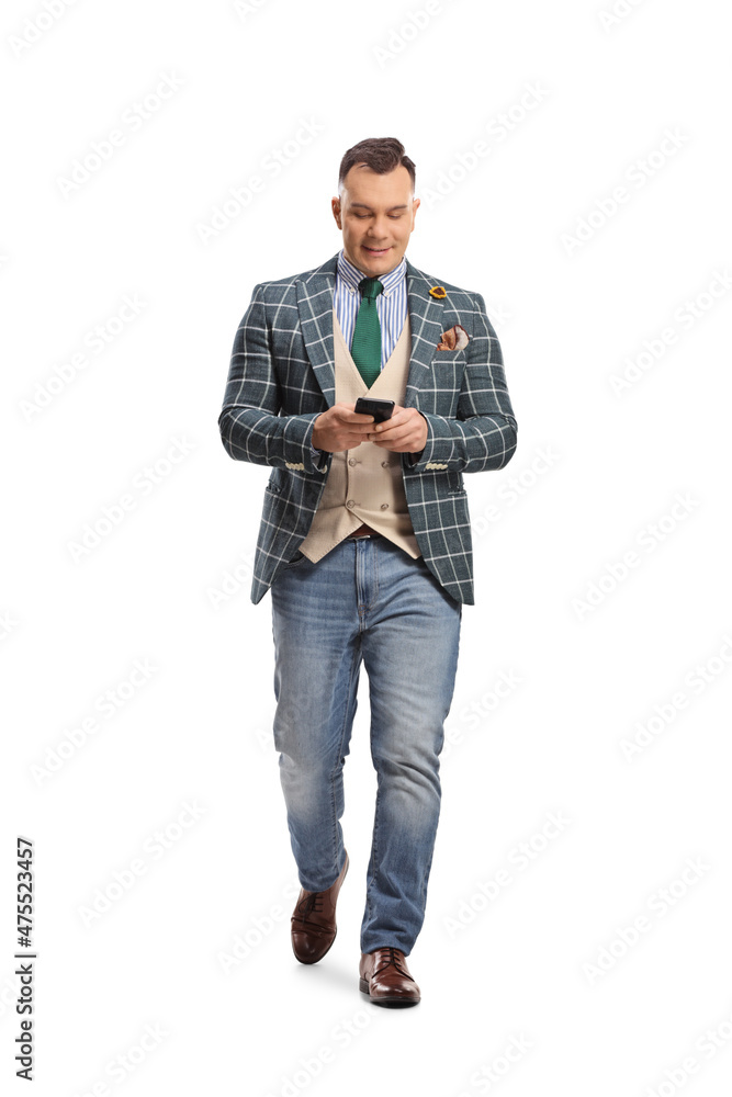 Fototapeta premium Full length portrait of a man in stylish suit and jeans walking and using a smartphone
