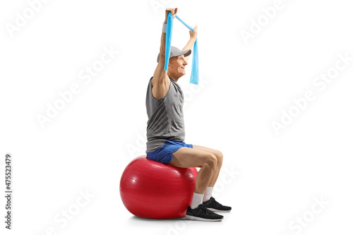 Side shot of an elderly man in sportswear exercising with an elastic band and a fitness ball