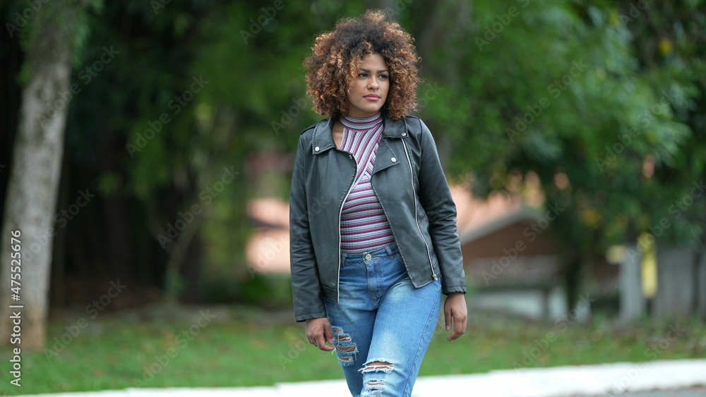 Fototapeta premium Young black woman walking forward. Confident Brazilian person walks outdoors