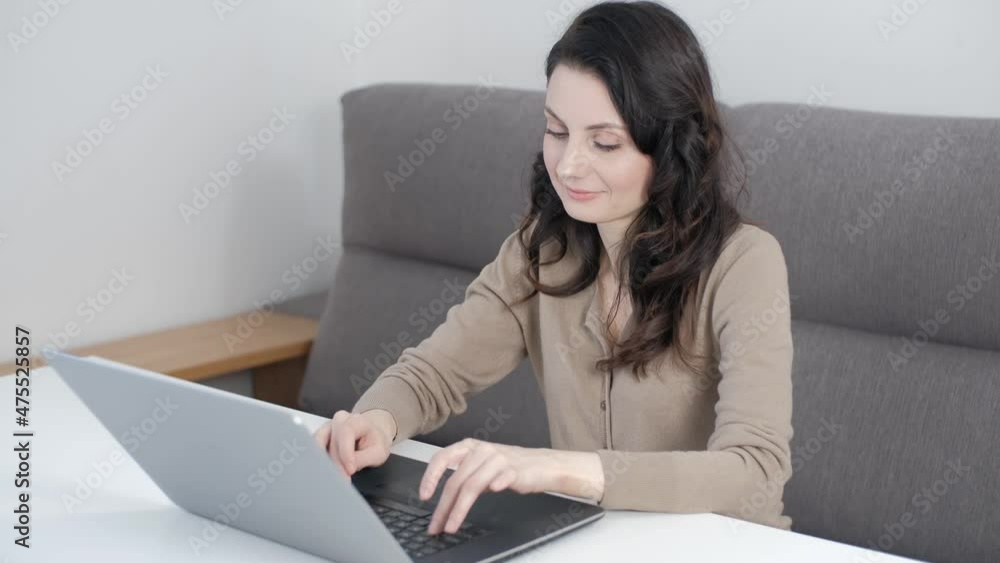 Free lance worker woman working from home using laptop computer. Freelancer typing text on notebook keyboard while sitting on couch behind white table in living room Free lance worker woman working from home using laptop computer. Freelancer typing text on notebook keyboard while sitting on couch behind white table in living room