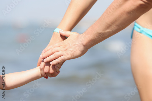 Family holding hands, mother father and child walking on coastline