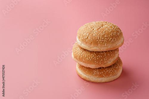 Three white wheat burger buns with sesame seeds on pink seamless surface, negative space