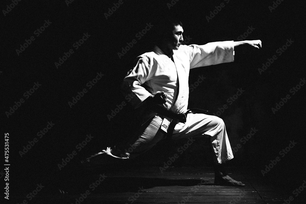 a young man, in a white kimano, shows the elements of karate in the studio on a black background