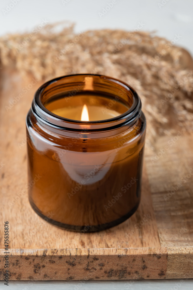 Burning aroma candle in a glass jar with the aroma of spices. Autumn atmosphere with dry reeds grass. Cosy lifestyle Burning aroma candle in a glass jar with the aroma of spices. Autumn atmosphere with dry reeds grass. Cosy lifestyle
