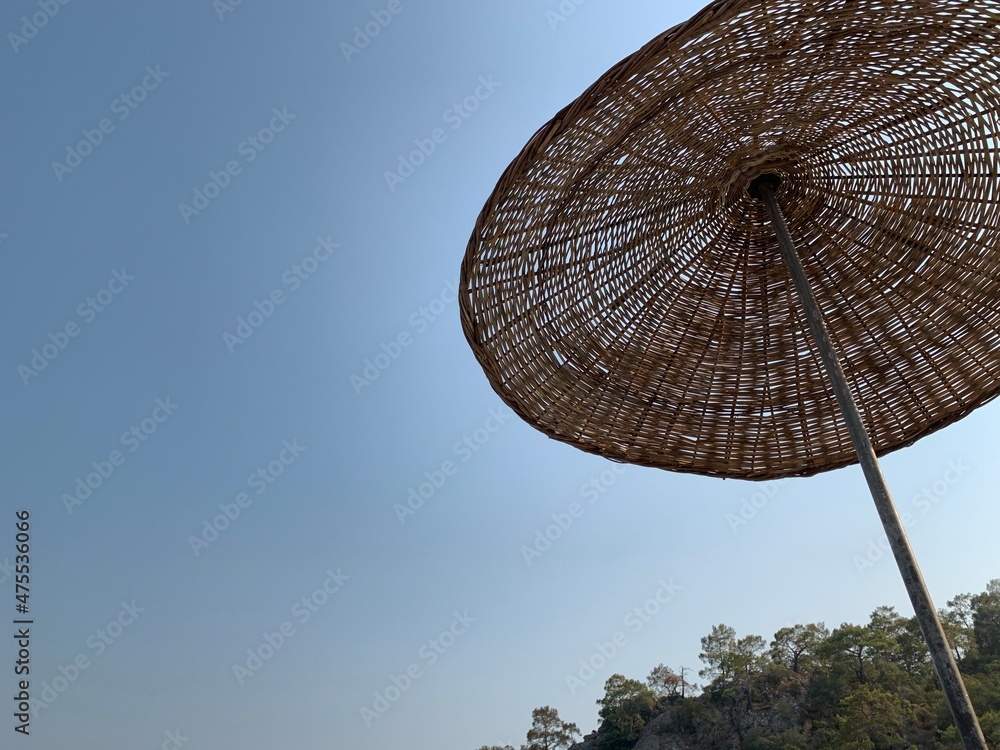 Fototapeta premium Umbrellas on the sandy beach against the background of the sky. Summer theme: relaxation in the sun. A straw umbrella by the sea.