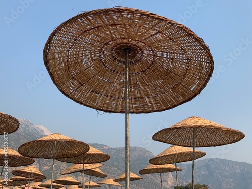 Umbrellas on the sandy beach against the background of the sky. Summer theme  relaxation in the sun  sea and mountains. A straw umbrella by the sea.